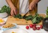 A person chops fresh kale surrounded by vibrant vegetables for a healthy meal preparation in a kitchen.