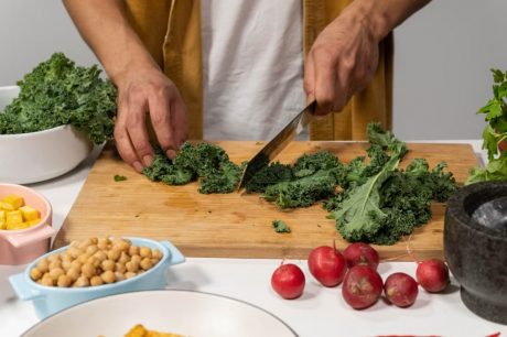 A person chops fresh kale surrounded by vibrant vegetables for a healthy meal preparation in a kitchen.
