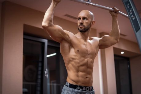 A bald, muscular man performing exercise on gym equipment indoors.